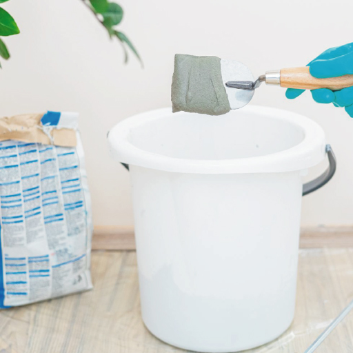 A person in blue gloves is preparing for a construction task by holding a bucket filled with cement.